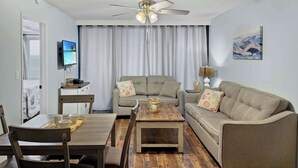 Een woonkamer met een plafondventilator, een televisie, een bank, een salontafel en een eethoek met stoelen en een tafel.
