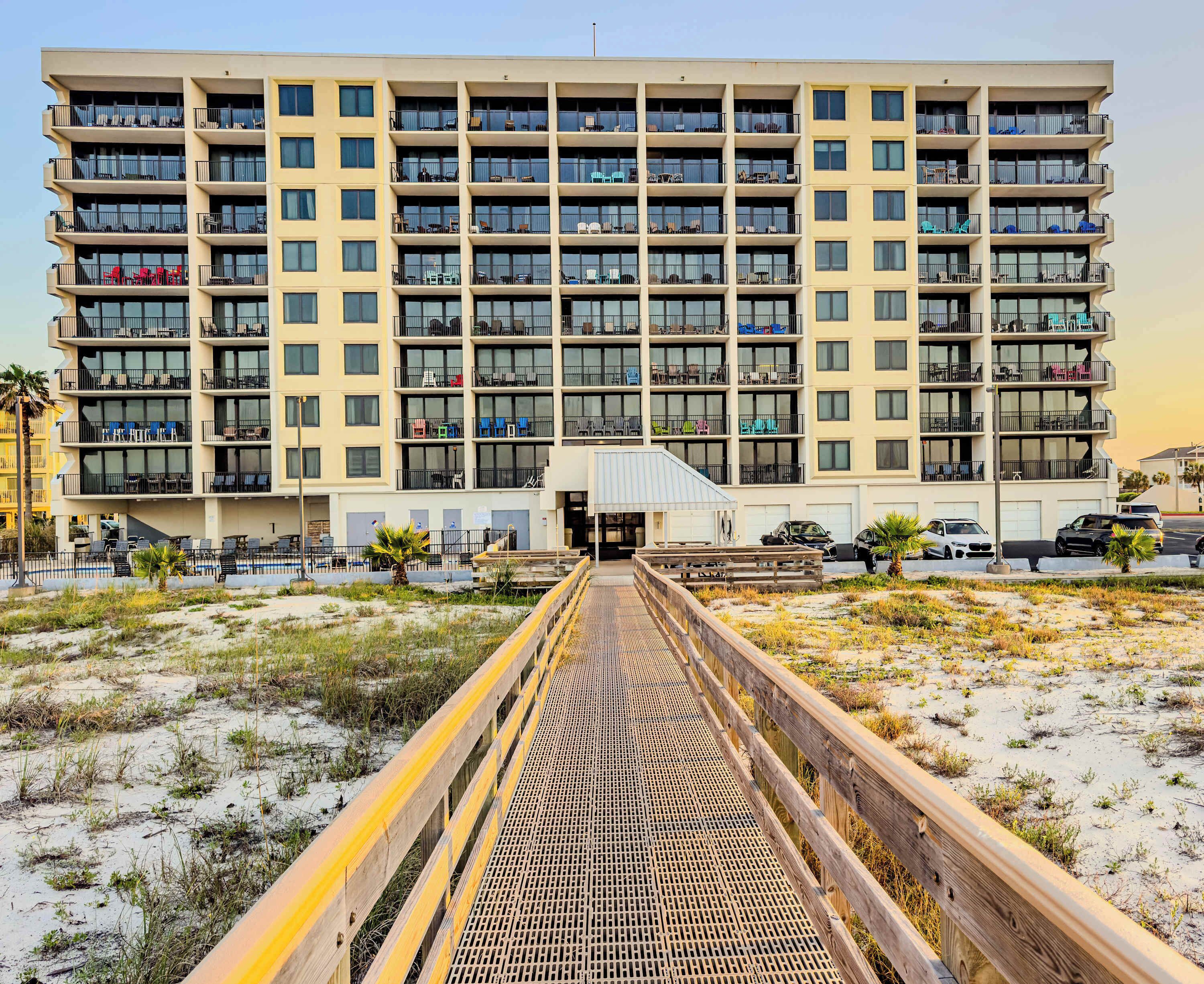 A multi-story hotel with balconies, a covered walkway, and a sandy beach area.