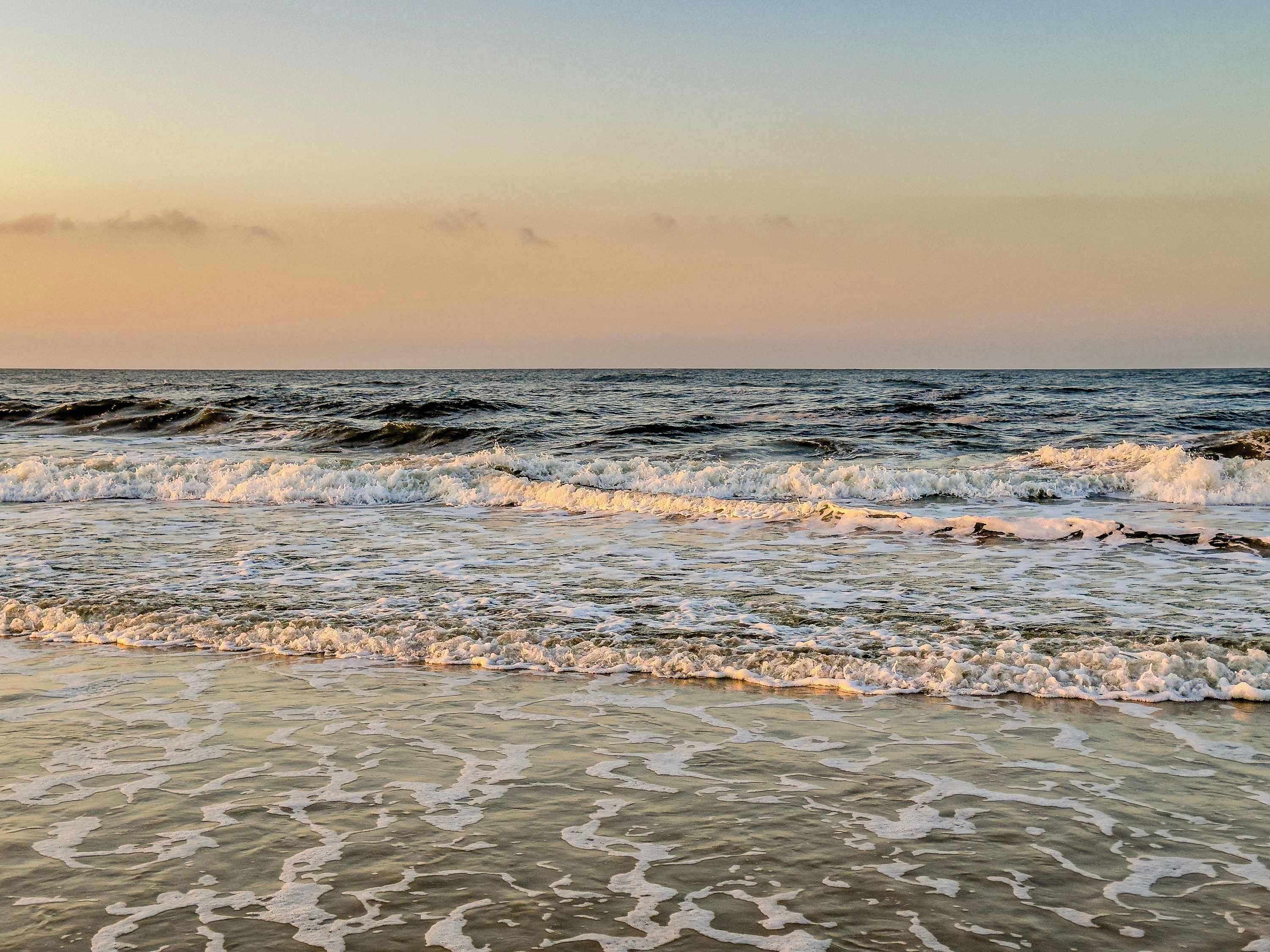 Ein Strand mit Wellen und Schaum, klarem Wasser und einem ruhigen Himmel.