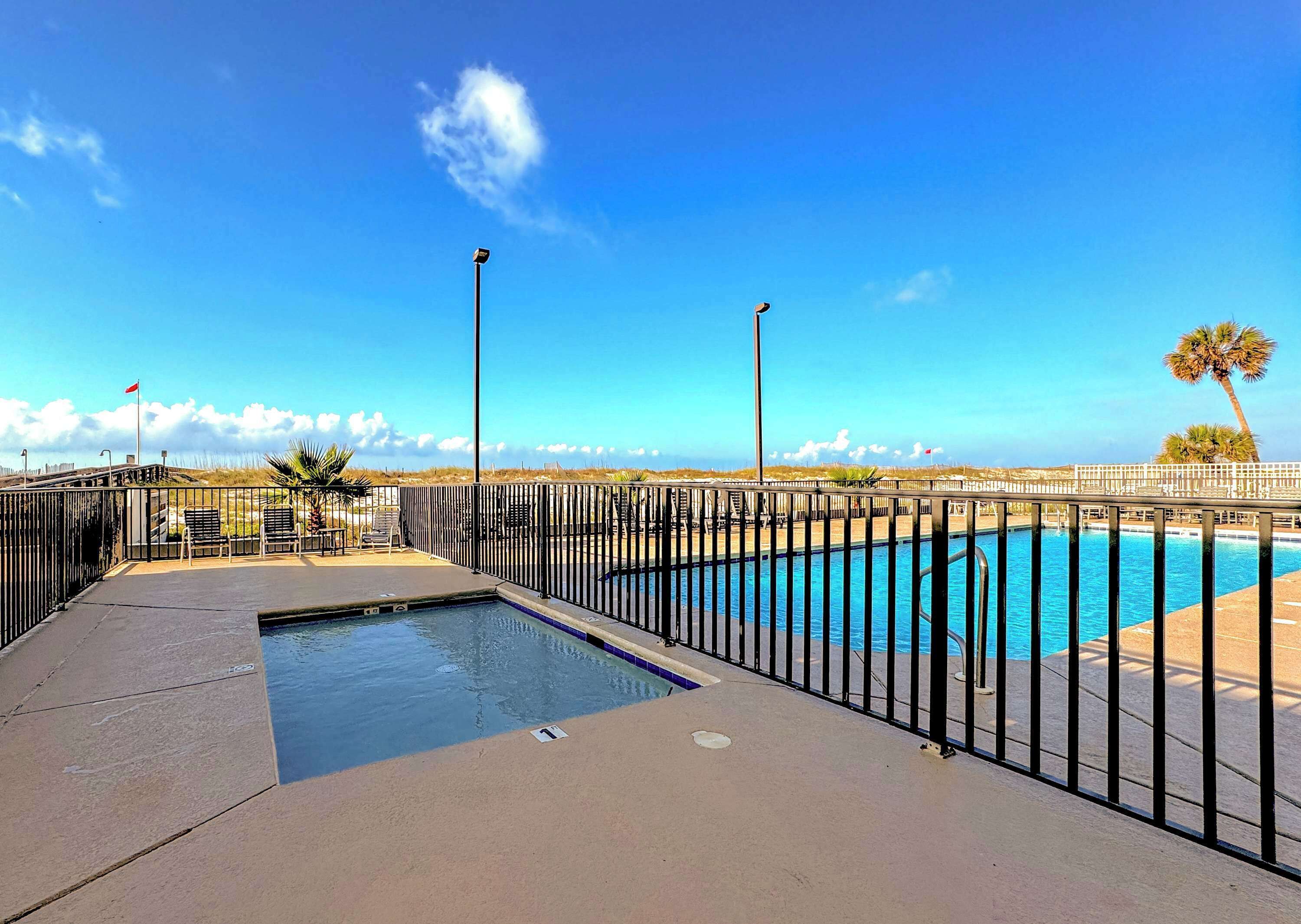 Ein Schwimmbecken mit schwarzem Metallzaun, einem kleinen Poolbereich und Blick auf Strand und Meer.