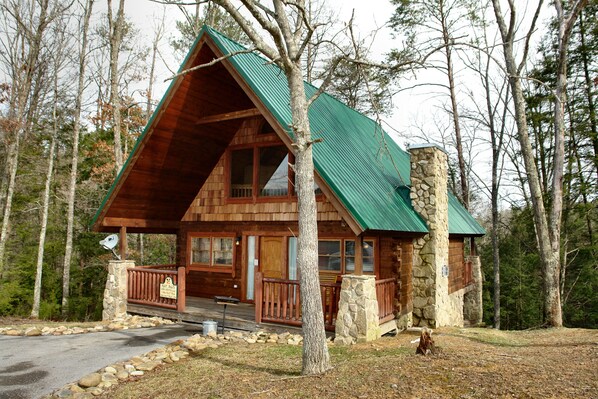 Une cabane en rondins avec une cheminée en pierre, une terrasse en bois et un porche doté d’une balustrade.