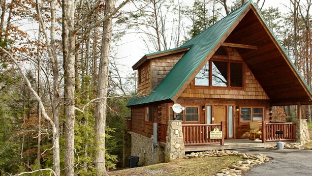 A cabin with a steeply pitched roof, stone foundation, and a porch with a stone railing. - Jacuzzi | Pigeon Forge | Pool Table | WiFi | Hot Tub (SEVIERVILLE)