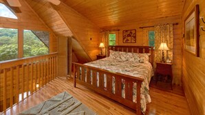 A wooden cabin bedroom with a bed, two bedside lamps, a window, and a view of greenery outside. - Jacuzzi | Pigeon Forge | Pool Table | WiFi | Hot Tub (SEVIERVILLE)