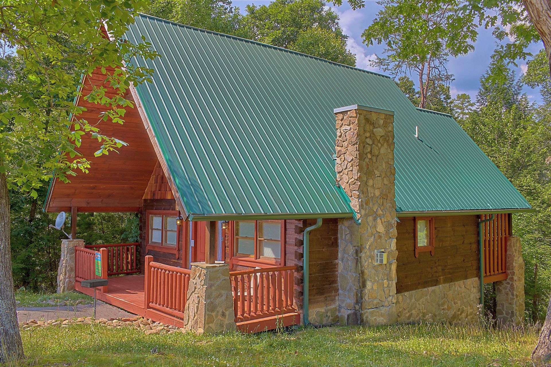 A cabin with a green metal roof, stone chimney, and a wooden porch with railings.