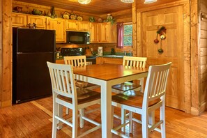 A wooden cabin kitchen with a central dining table, white chairs, a black refrigerator, a microwave, and a stove. - Jacuzzi | Pigeon Forge | Pool Table | WiFi | Hot Tub (SEVIERVILLE)