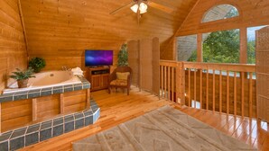 A wooden cabin interior with a wooden deck, a bathtub, a television, and a ceiling fan. - Jacuzzi | Pigeon Forge | Pool Table | WiFi | Hot Tub (SEVIERVILLE)