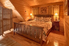 A wooden room with a bed, two bedside lamps, and a window with curtains. - Jacuzzi | Pigeon Forge | Pool Table | WiFi | Hot Tub (SEVIERVILLE)
