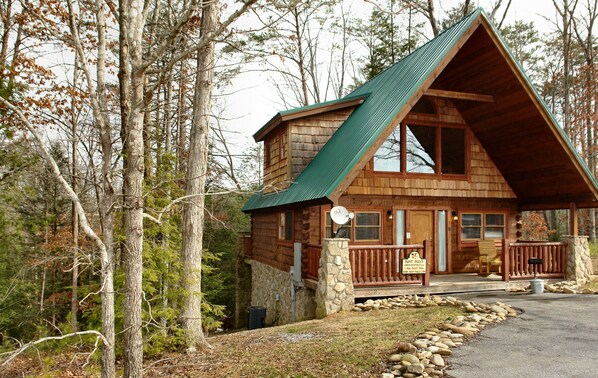 A cabin with a steeply pitched roof, stone foundation, and a porch with a stone railing.