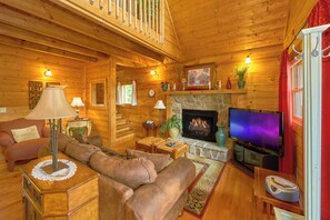 A cozy log cabin interior with a fireplace, a television, and a comfortable seating area.