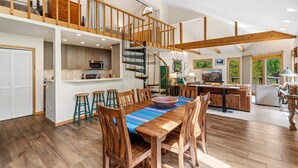 Un vaste espace de vie comprenant un escalier en bois, une table à manger avec des chaises et un coin cuisine.