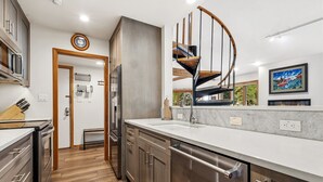 Une cuisine moderne dotée d’appareils électroménagers en acier inoxydable, d’un escalier en bois et offrant une vue sur l’extérieur.