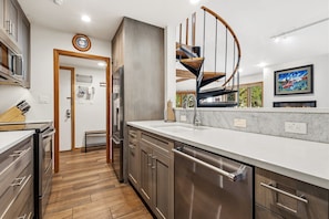 Una cocina moderna con electrodomésticos de acero inoxidable, una escalera de madera y vistas al exterior.