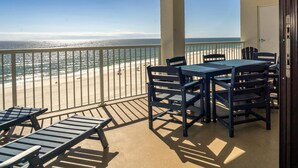 A balcony with a table and chairs, overlooking a beach with people and a clear sky. - Summer House 703B - Great Beachfront Condo with Huge Balcony & Amazing Views! (Orange Beach)