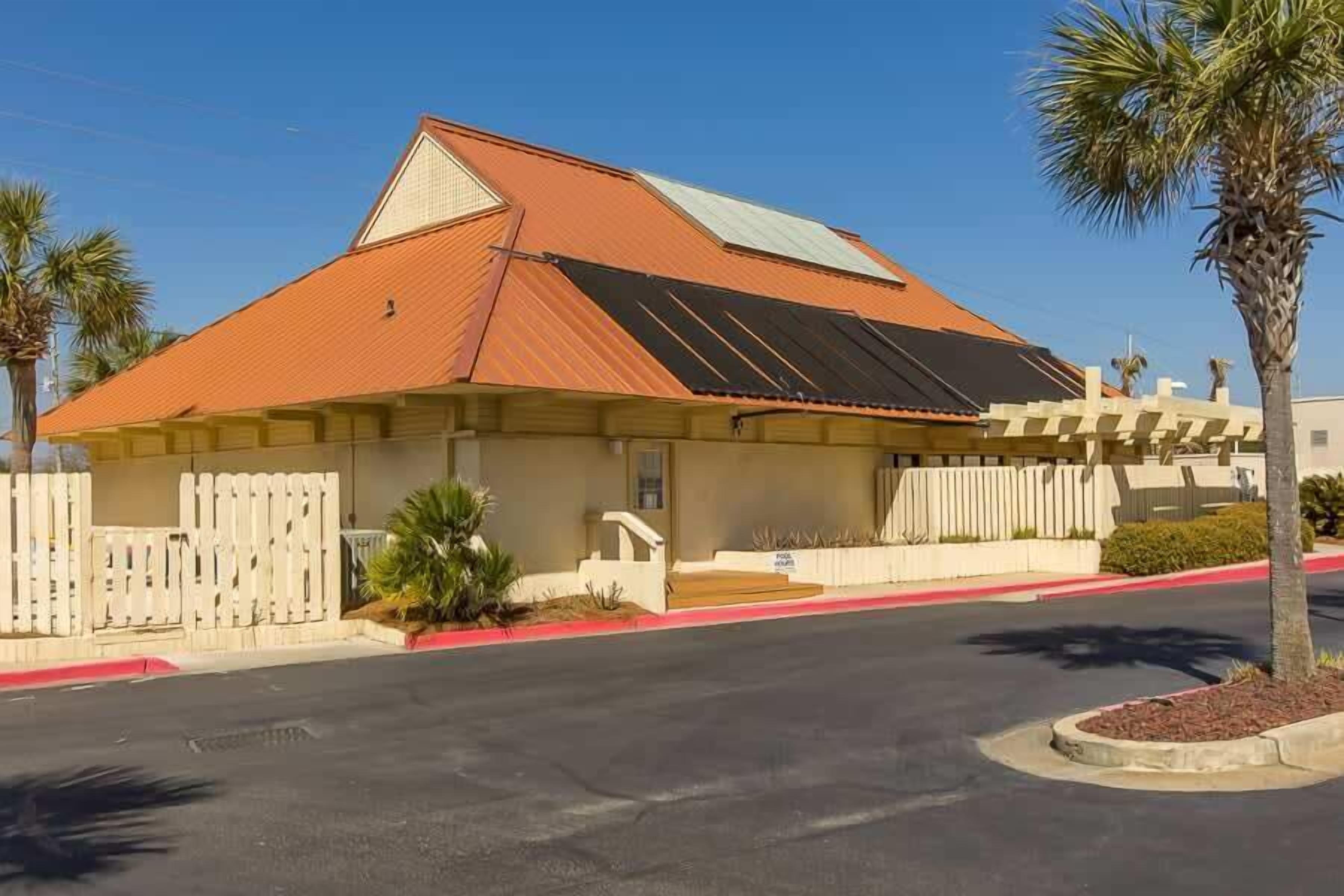 A single-story building with a red roof, a white picket fence, and a palm tree in the foreground.