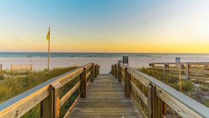 A wooden boardwalk leading to a beach with a flag and a signboard. - Summer House 703B - Great Beachfront Condo with Huge Balcony & Amazing Views! (Orange Beach)