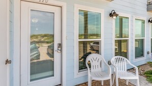 Une maison avec le numéro « 110 » sur la porte, une porte-fenêtre coulissante et deux chaises en plastique blanches à l’extérieur.