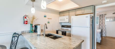 A kitchen with a granite countertop, stainless steel appliances, and a small dining area with stools.