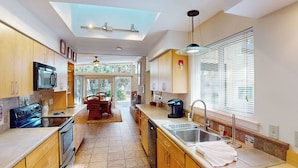 A modern kitchen with wooden cabinets, a black microwave, a stove, and a dining area with a table and chairs.