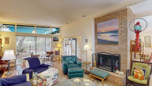 A spacious living room with a large window, a fireplace, and a variety of seating options including a sofa, armchair, and ottoman.