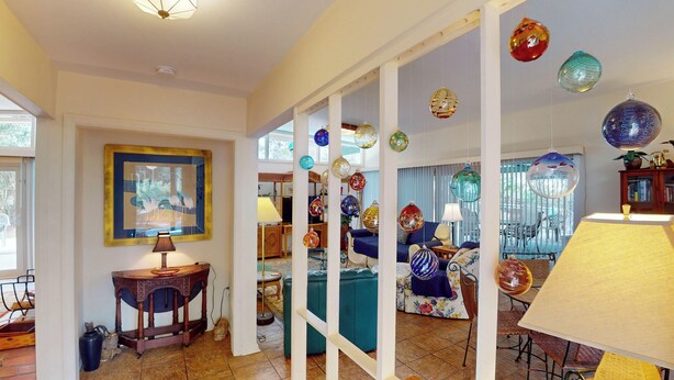 A room with a wooden table, a lamp, a framed picture, and a glass partition with hanging ornaments.