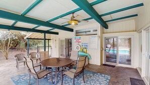 A covered patio with a round table and chairs, a ceiling fan, and pool safety signs.
