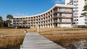 Un hotel moderno con una facciata curva, numerosi balconi e una passerella in legno che conduce a una zona verde.