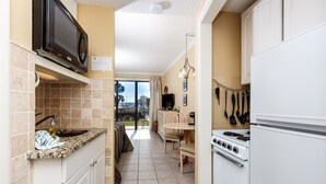 Una cucina compatta con microonde, fornello e lavello. C'è un'area pranzo con tavolo e sedie, e una vista all'esterno tramite una porta vetrata.