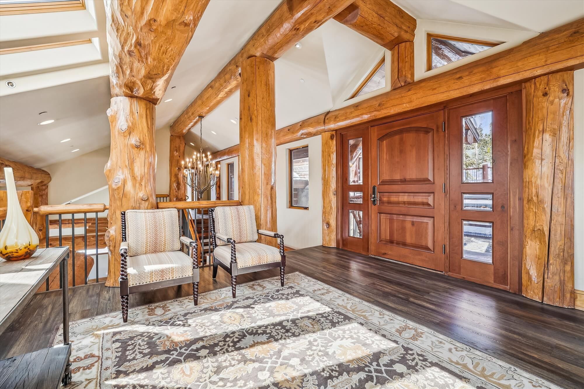 A spacious room with wooden beams, a large wooden door, and a patterned rug.