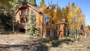 A rustic log cabin with multiple balconies and a porch, surrounded by autumn foliage. - Exquisite Home with Ski-In Access, PRIVATE HOT TUB, Stunning Views. FOUR (Breckenridge)