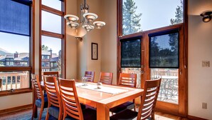 A dining area with a wooden table and chairs, large windows, and a chandelier. - Exquisite Home with Ski-In Access, PRIVATE HOT TUB, Stunning Views. FOUR (Breckenridge)