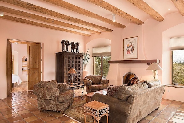 A living room with a sofa, armchairs, a wooden cabinet, and a large window.