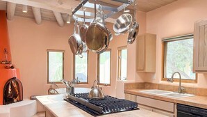 Een moderne keuken met een centraal eiland, hangende pannen, een fornuis en een open haard.