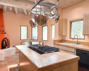 A modern kitchen with a central island, hanging pots, a stove, and a fireplace.