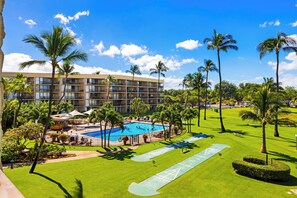 Un hotel con piscina rodeado de palmeras y un césped bien cuidado.