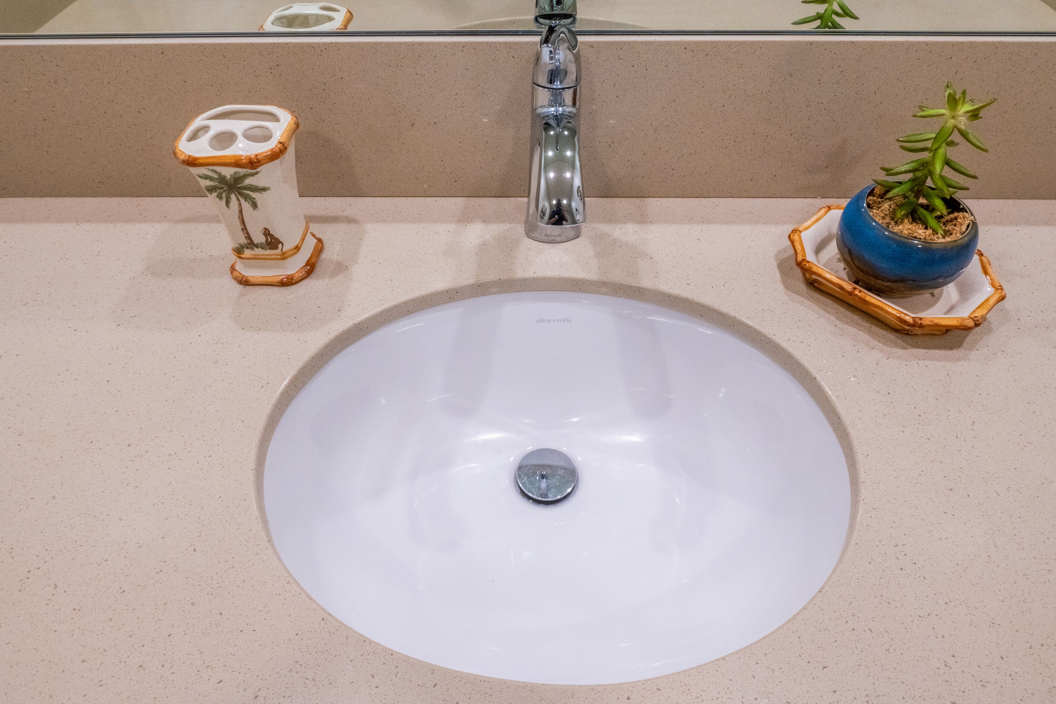 A bathroom sink with a white basin, a chrome faucet, a decorative vase with a plant, and a small round mirror.