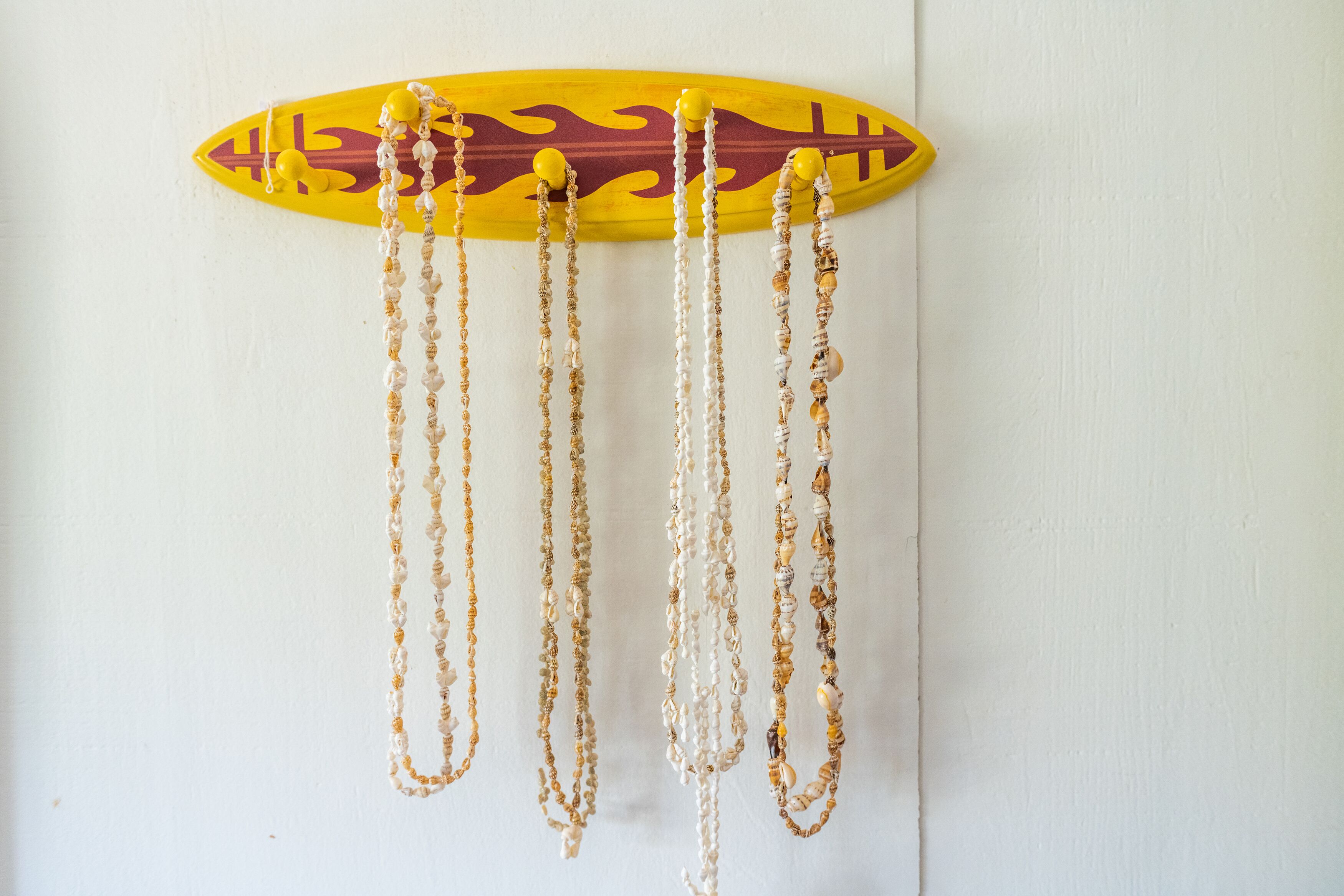 A surfboard-shaped wall hanging with multiple necklaces.