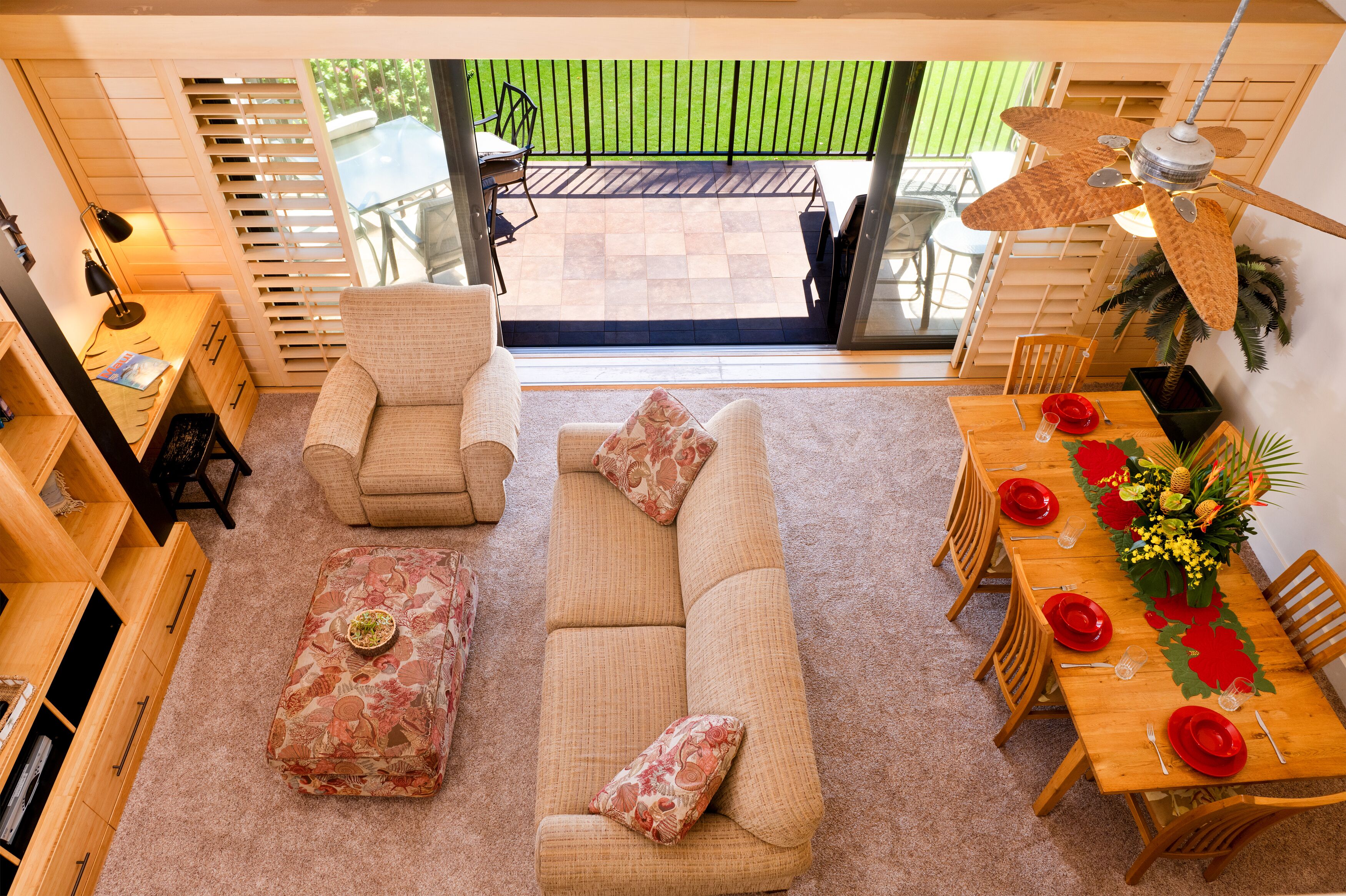 A cozy living room with a sofa, armchair, and ottoman, a dining area with a table set for four, and a balcony with a patio table and chairs.