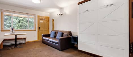 Una habitación con un sofá de cuero marrón, una puerta de madera, una pared blanca y un armario grande de color blanco.
