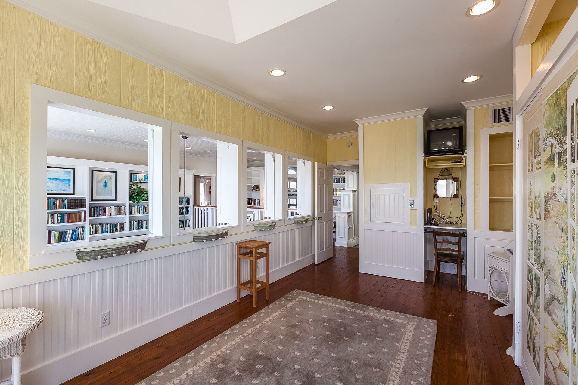 A spacious hallway with a wooden floor, white walls, and a large window on the left.