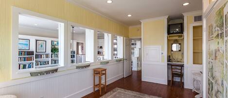 A spacious hallway with a wooden floor, white walls, and a large window on the left.