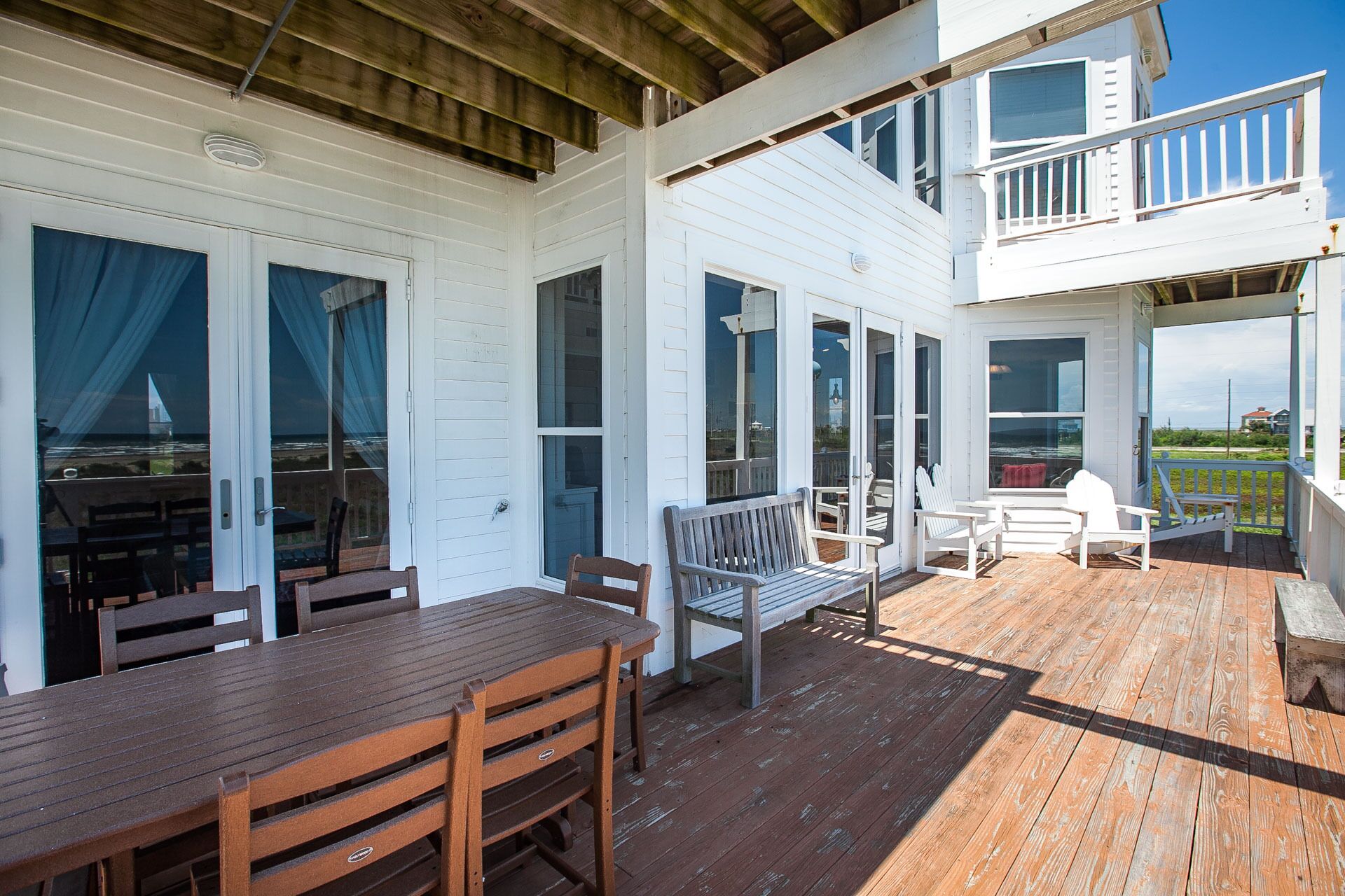 Une terrasse extérieure couverte, aménagée avec du mobilier en bois, notamment une table, des chaises et un banc.