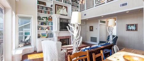 A spacious living area with a fireplace, bookshelves, a dining table, and a view of the outdoors.
