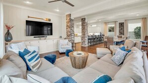 A spacious living room with a large sofa, a television, and a dining area in the background.