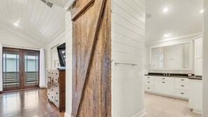 A spacious room with a wooden door, white walls, and a kitchen area with white cabinets and a black countertop.