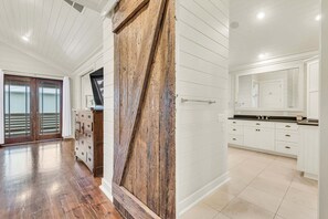 A spacious room with a wooden door, white walls, and a kitchen area with white cabinets and a black countertop.