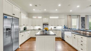 A modern kitchen with white cabinetry, a central island, stainless steel appliances, and a stone backsplash.