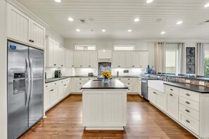 A modern kitchen with white cabinetry, a central island, stainless steel appliances, and a stone backsplash.