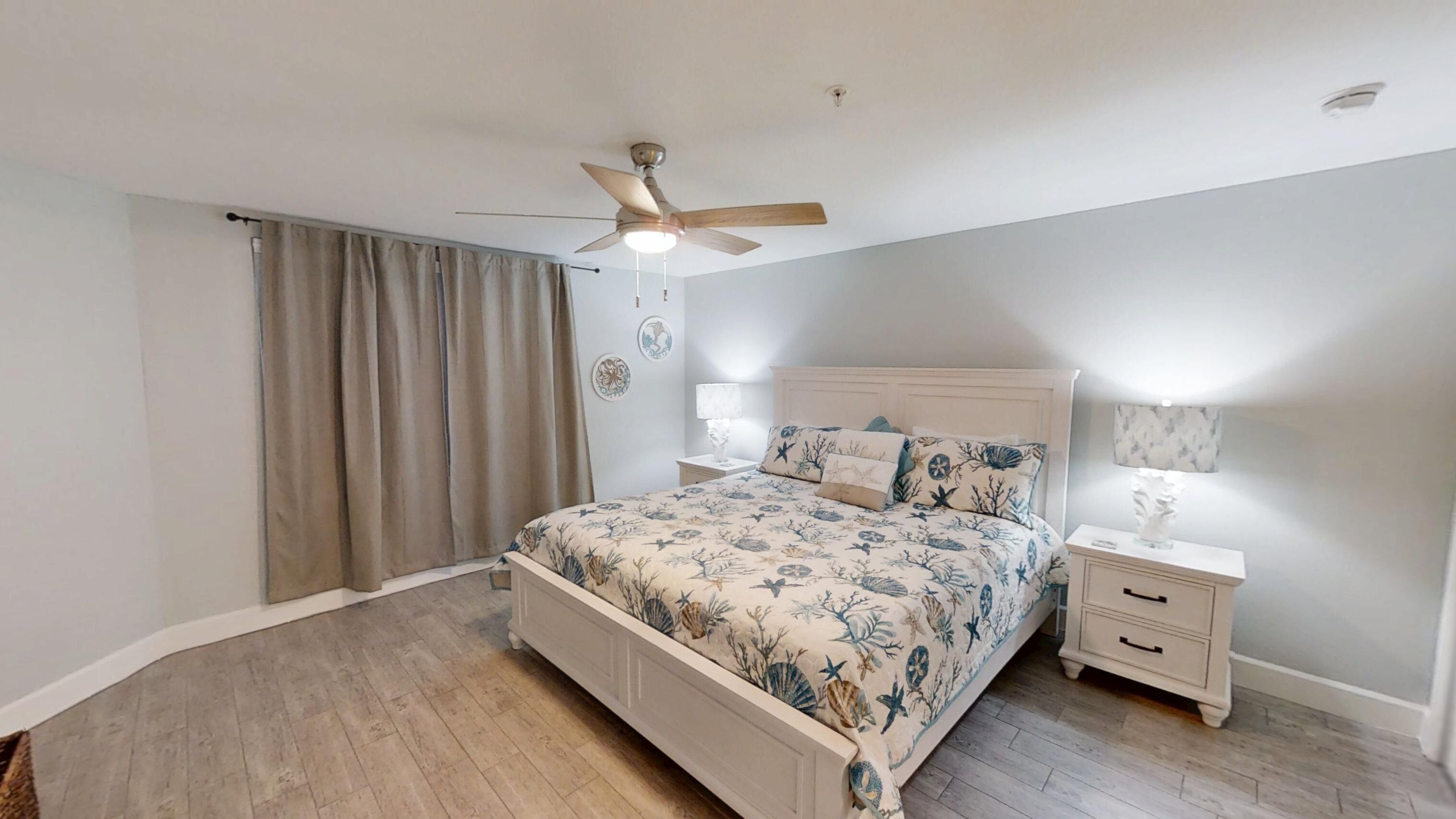 A bedroom with a bed, nightstands, a ceiling fan, and a window with curtains.