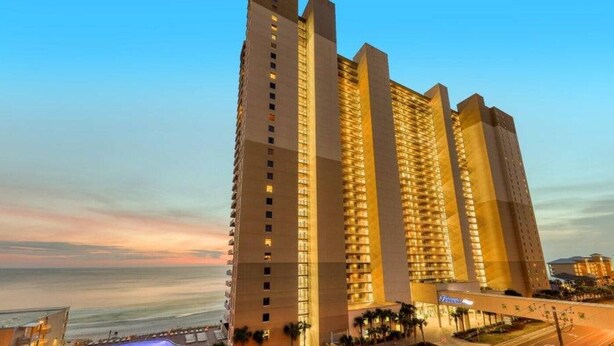A high-rise hotel with multiple floors, a prominent entrance, and a view of the ocean. - Amazing Deluxe Gulf Master! Free Beach Service! Free Golf & Activities Daily! (Panama City Beach)