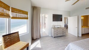 A bedroom with a view of the beach, a dresser, a television, and a bathroom with a sink and mirror. - Amazing Deluxe Gulf Master! Free Beach Service! Free Golf & Activities Daily! (Panama City Beach)